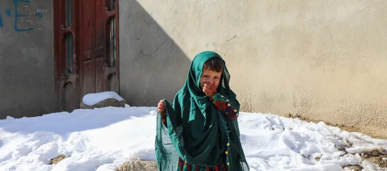Rahima, 4 jaar, staat in de bijtende kou voor haar huis in Nuristan, Afghanistan.