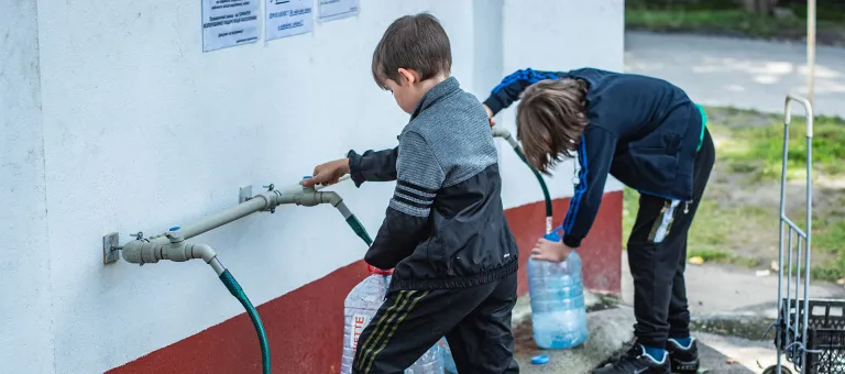 Kinderen vullen een drinkbus aan een watertappunt geïnstalleerd door UNICEF in Mykolaiv, Oekraïne