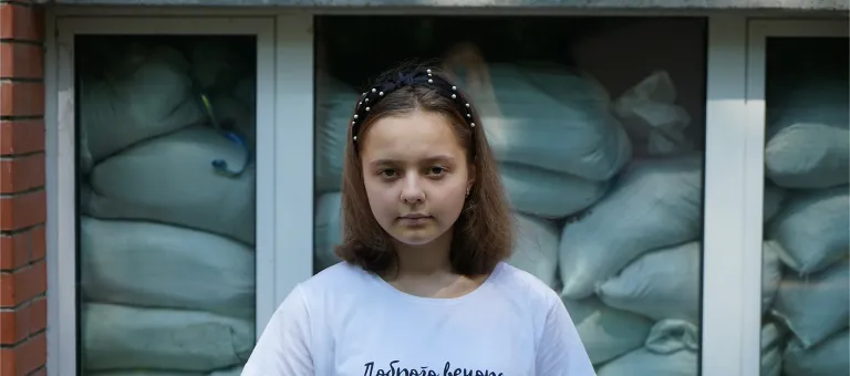 Sofia, 15 jaar, staat voor haar school in Pushcha-Voditsa, Oekraïne. Achter het raam zijn zandzakken opgestapeld om de school te beschermen als er beschietingen zijn. 