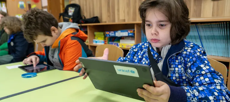 Hlib, 8 jaar, uit Cherson, volgt de lessen op de nieuwe tablet die hij heeft gekregen met de steun van UNICEF. Nu hoeven hij en zijn broers niet meer af te wisselen op de enige smartphone die ze hebben in de familie, en missen ze nooit meer de schoollessen. © UNICEF/UN0839492/Filippov