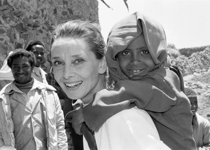 UNICEF Goodwill Ambassador Audrey Hepburn smiles as she carries a child on her back, in the northern town of Mehal Meda in Shoa Province. Ms. Hepburn was visiting a food distribution centre in the town.
