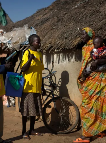 Social mobilizer Dor Gawar and vaccinator Nyakuoth Chuol, 15, speak with Aluk Chol, holding her 2-year-old son, Mayol Deng, outside her home, in the Chilak Returnee Centre, in the town of Rubkona, Unity State. Nyakuoth is carrying a 'cold box' filled with polio vaccines. 'Cold boxes' play a critical role in preserving the ‘cold chain’, the series of temperature controls required to maintain vaccine potency from manufacture through inoculation. The centre – run by the Government with support from UNICEF and 